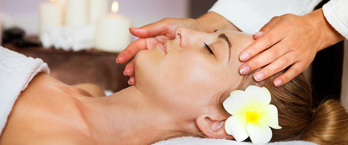 Masaje facial con manos y flor blanca en un spa, mujer recostada