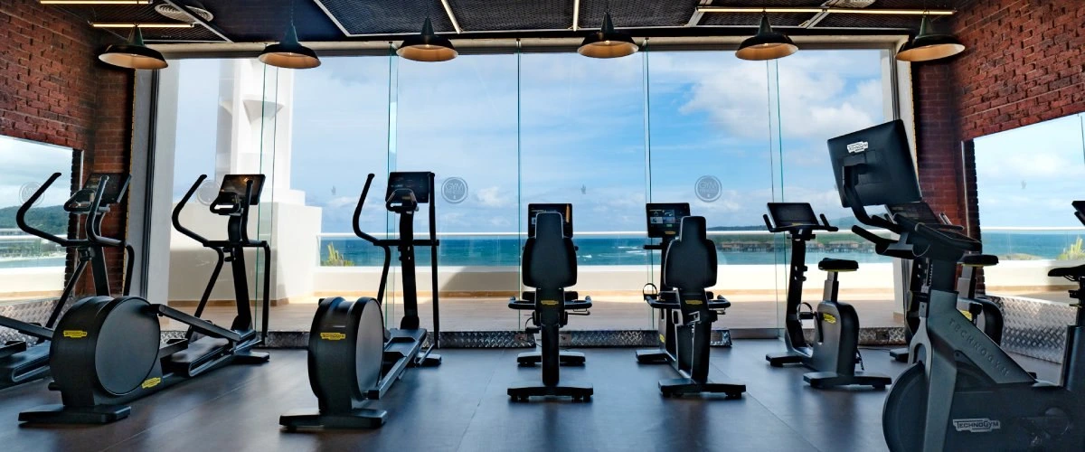 Gimnasio moderno con m&aacute;quinas de cardio frente a ventanales al mar.