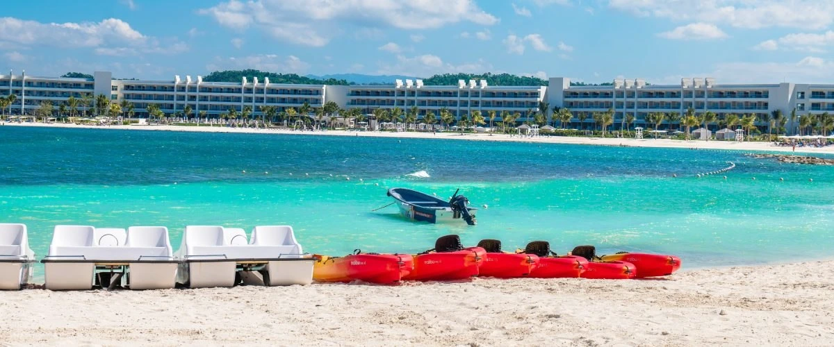 Playa tropical con kayak rojos y botes junto a un hotel frente al mar azul