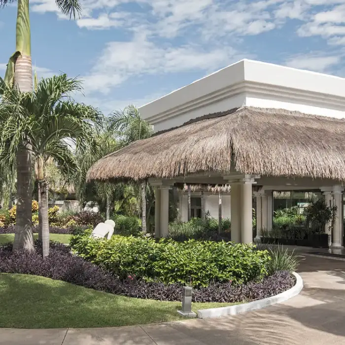 Jard&iacute;n tropical con palmeras y pabell&oacute;n de techo de paja blanca junto a piscina