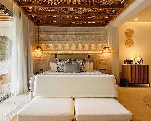 Dormitorio con cama grande, iluminaci&oacute;n c&aacute;lida y cabecero de madera.
