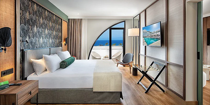 Habitaci&oacute;n de hotel moderna con cama, sill&oacute;n y vista al mar por el arco