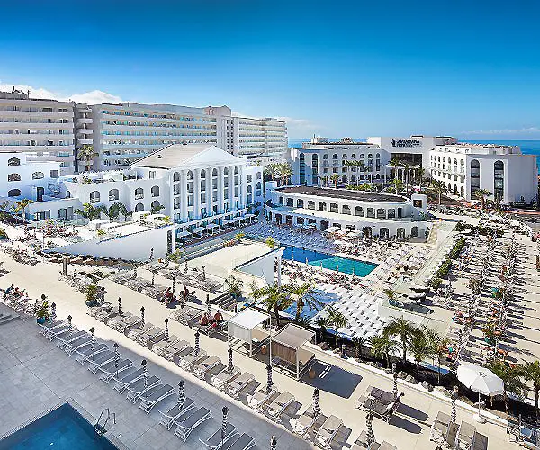 Complejo hotelero frente al mar con piscinas y edificios blancos.
