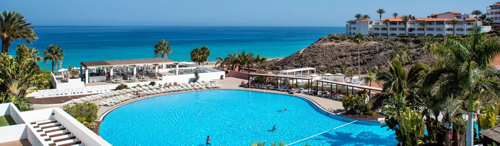 Hotel junto al mar con piscina azul y palmeras, vista panor&aacute;mica