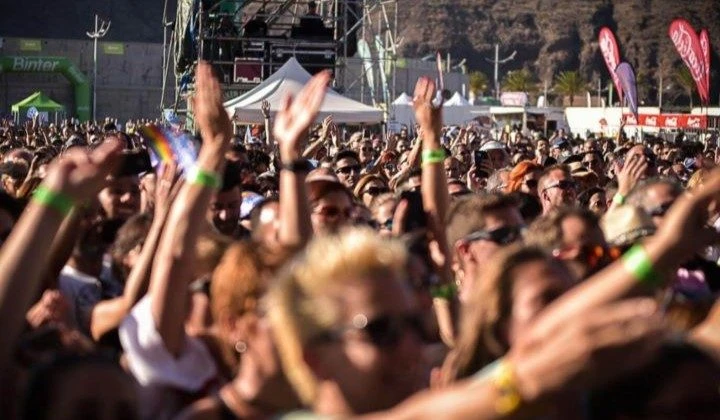 Multitud en un festival musical al aire libre con escenario y banderas rojas