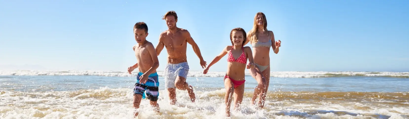 Familia corriendo en la playa con el agua a salpicaduras, al sol
