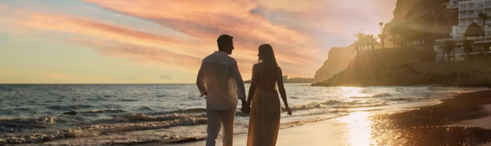 Pareja caminando por la playa al atardecer, tomada de la mano