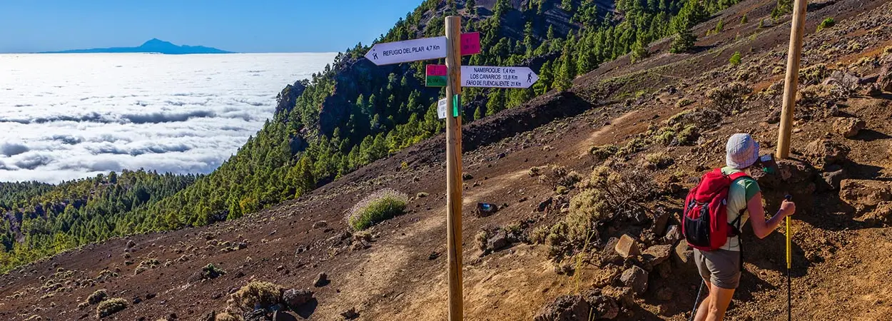 Senderista con mochila en ruta de monta&ntilde;a, se&ntilde;alizaci&oacute;n y lago al fondo.