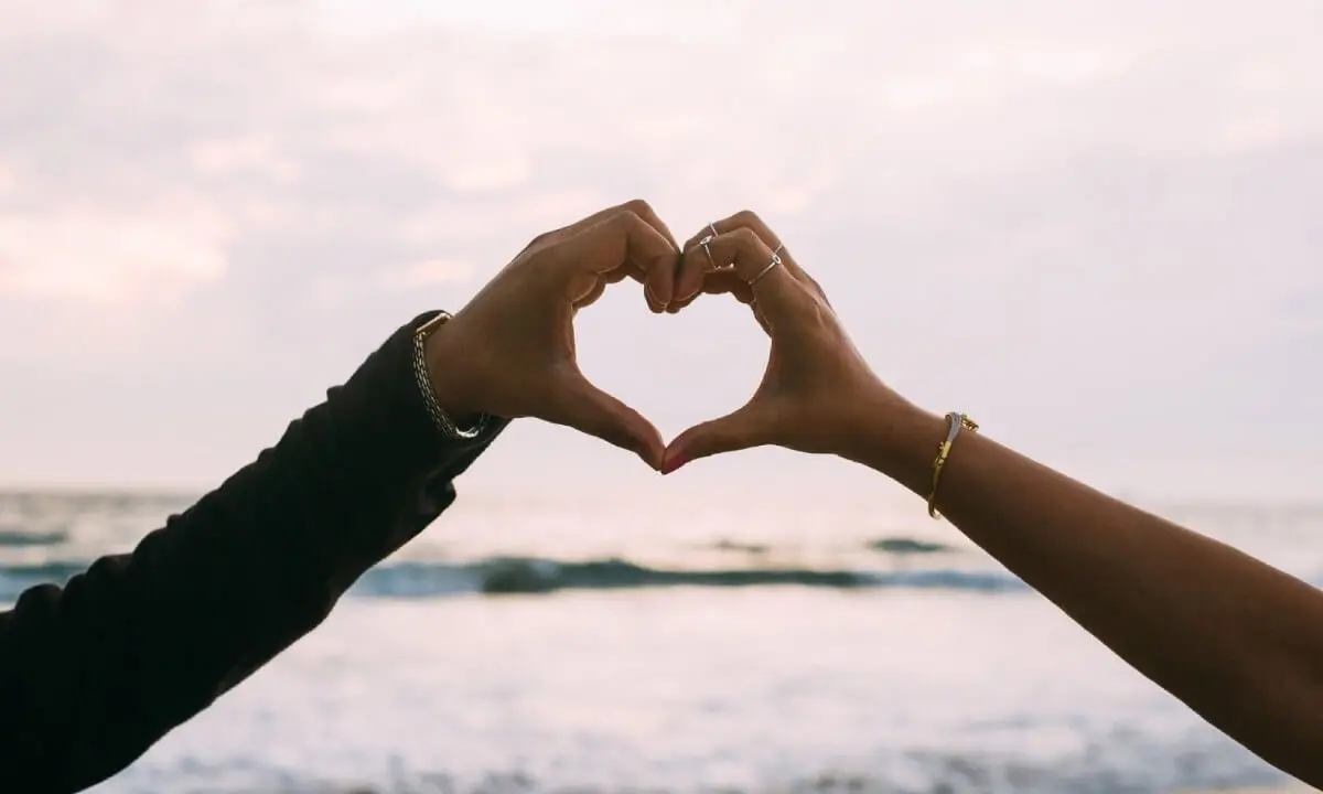 Dos manos forman un coraz&oacute;n en la playa con el mar al fondo