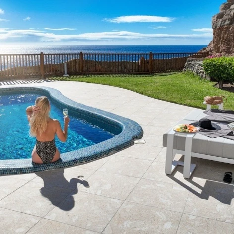 Mujer en piscina junto al mar, terraza con tumbona y vistas al acantilado