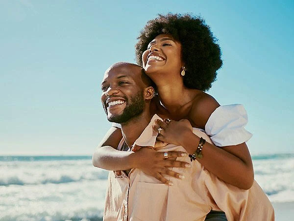 Pareja feliz abrazada en la playa, sonriendo al sol.
