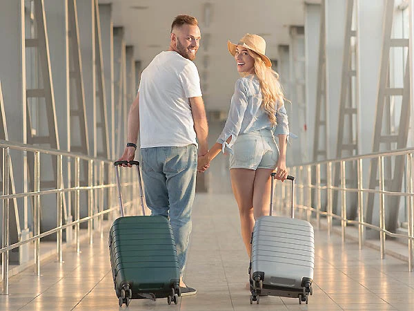 Pareja caminando en aeropuerto con maletas verdes y grises.