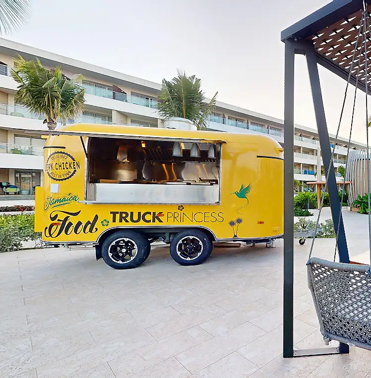 Cami&oacute;n amarillo de comida &ldquo;Truck Princess&rdquo; en hotel, con palmeras y patio.