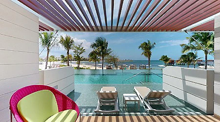 Piscina frente al mar, palmeras y sillas en terraza con techo de madera.