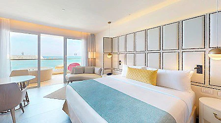 Habitaci&oacute;n de hotel luminosa con cama, sill&oacute;n y vista al mar.
