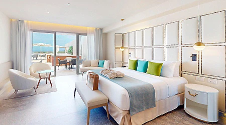 Habitaci&oacute;n de hotel moderna con cama y sillones junto a ventanal.