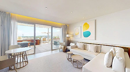 Sala de hotel moderna con sof&aacute;, mesa redonda y ventanal con balc&oacute;n