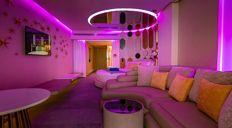 Sala moderna con luces moradas, sof&aacute; y decoraci&oacute;n met&aacute;lica en el techo.