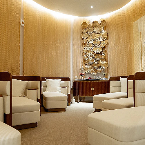 Sala de spa moderna con sillones blancos y pared decorativa dorada.