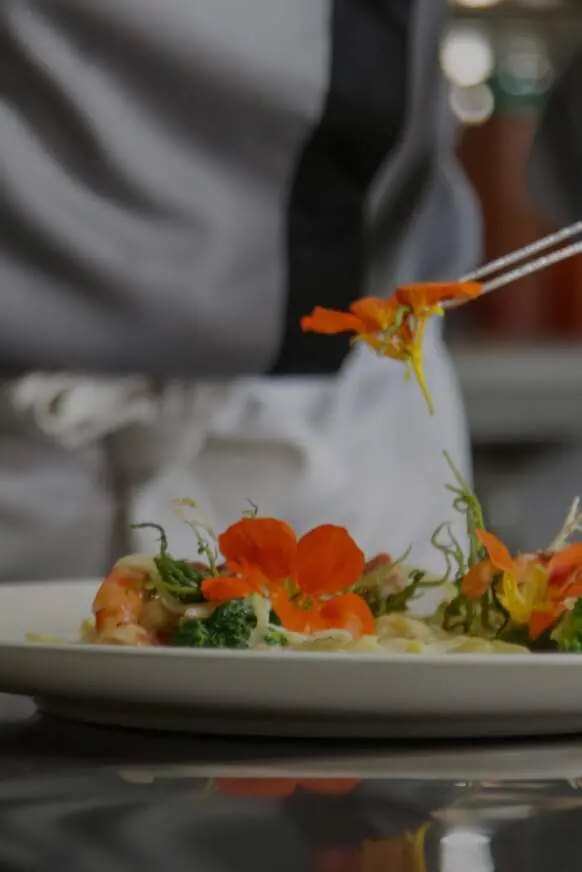 Plato con flores naranjas y verdes adornando la comida, fondo desenfocado.