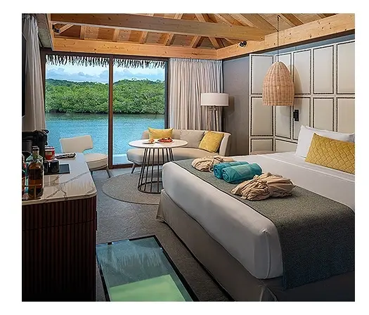 Habitaci&oacute;n hotelera con cama y vista al lago, terraza y cortinas.