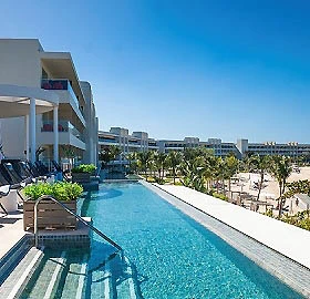 Piscina al aire libre frente al mar con edificios y palmeras al fondo