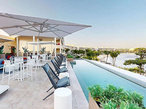 Terraza con piscina y tumbonas junto al mar, bajo sombrillas blancas.