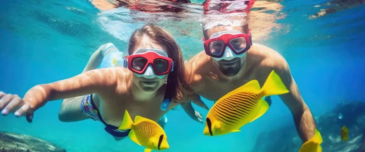 Dos nadadores con gafas y aletas en el mar, con peces alrededor.