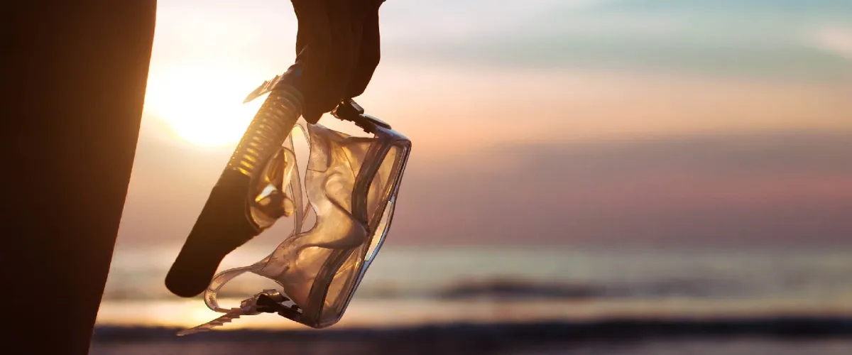 Persona en la playa con tel&eacute;fono m&oacute;vil reflejando el atardecer