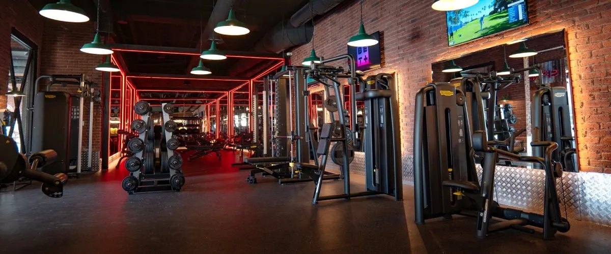Gimnasio moderno con m&aacute;quinas de pesas y luces rojas en ladrillo.
