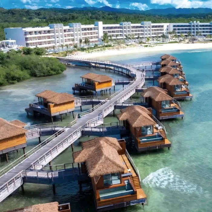 Hotel con bungalows sobre el agua y puente hacia la playa en la costa tropical.