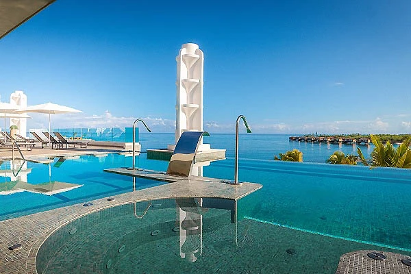 Piscina junto al mar con tumbonas y sombrillas, cielo azul.
