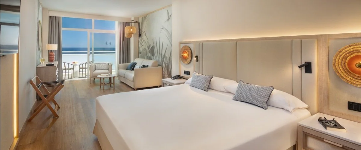 Dormitorio moderno con cama blanca y vista al mar desde un ventanal