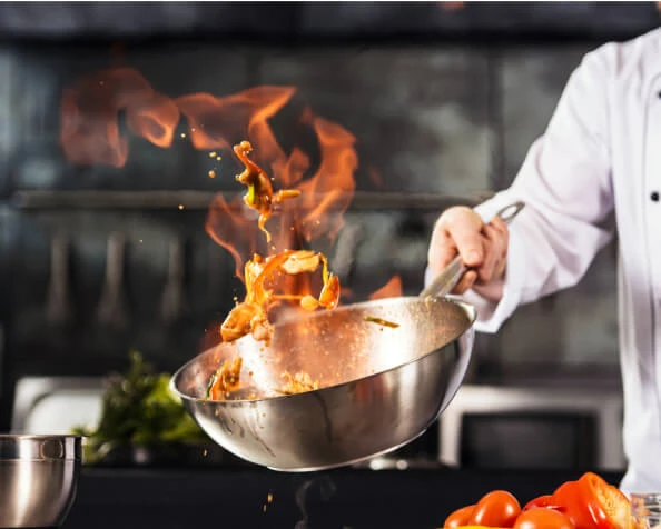 Chef salteando en sart&eacute;n con llamas y verduras al lado