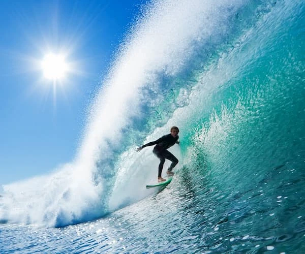 Surfista monta una ola bajo el sol, sobre el mar azul.
