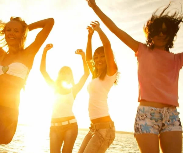 Grupo de j&oacute;venes bailando en la playa al atardecer