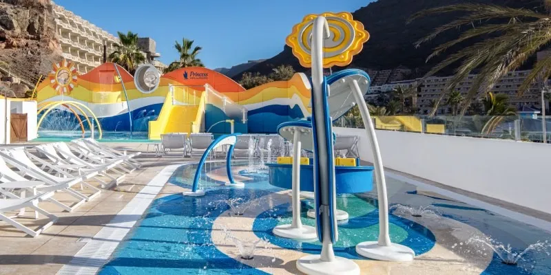 Piscina infantil con toboganes y sillas blancas en complejo tur&iacute;stico