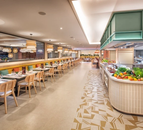 Interior de restaurante moderno con mesas, barra y buffet de verduras.