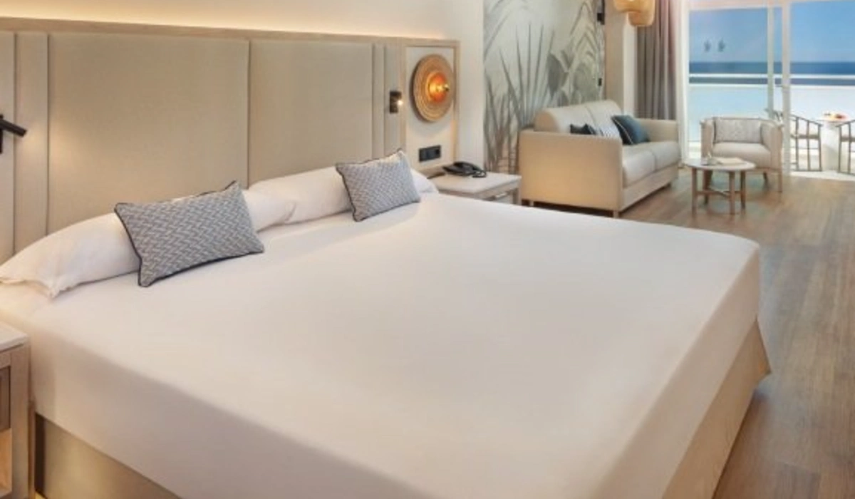 Dormitorio con cama grande, sof&aacute;s y balc&oacute;n con vista al mar