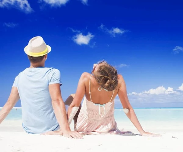 Pareja tomando el sol en la playa bajo un cielo azul con nubes