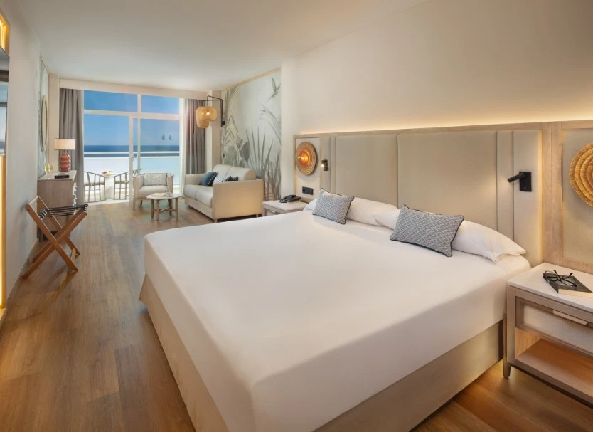 Dormitorio moderno con cama king, almohadas y vista al mar por la ventana