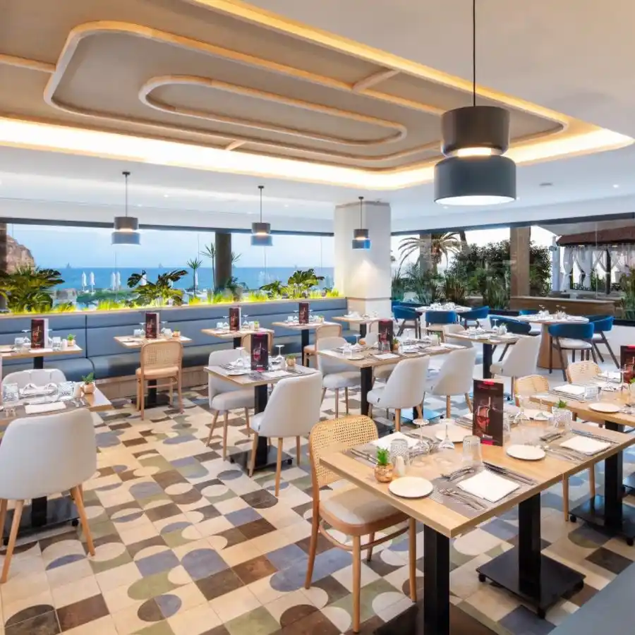 Restaurante al aire libre con mesas, sillas y vista al mar, iluminaci&oacute;n moderna