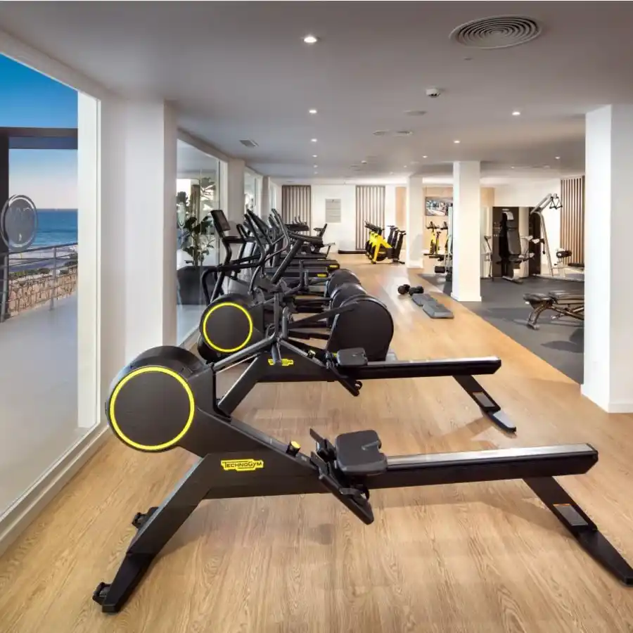 Gimnasio moderno con m&aacute;quinas el&iacute;pticas y vistas al mar por ventanales