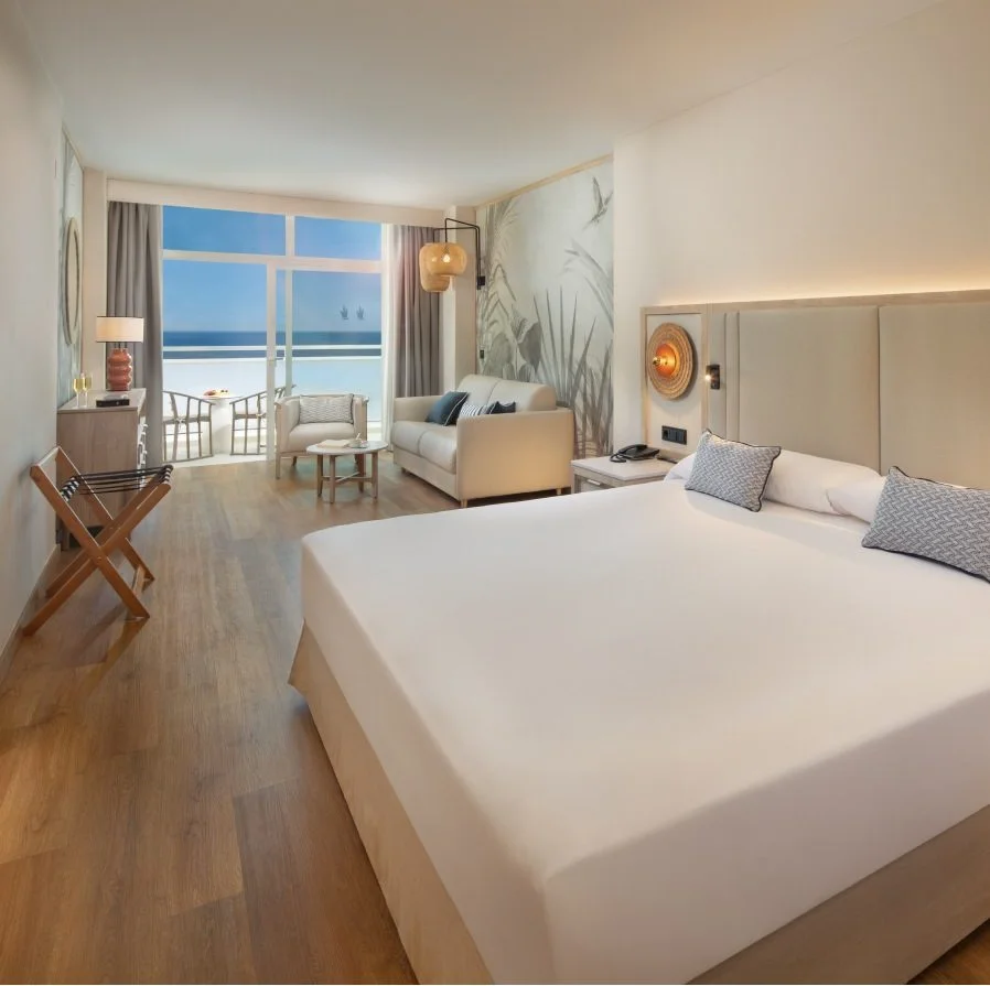 Suite moderna con cama, sill&oacute;n y vista al mar desde el balc&oacute;n.