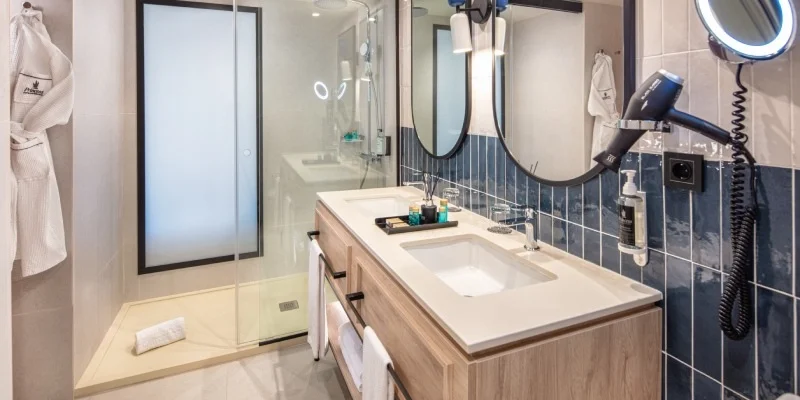 Ba&ntilde;o moderno con lavabo doble, ducha de vidrio y espejo con luces.