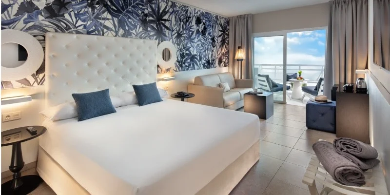 Habitaci&oacute;n de hotel moderna con cama grande, sof&aacute;s y balc&oacute;n, vista al mar