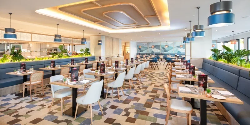 Comedor moderno con mesas, luces colgantes y suelo de mosaico en hotel.