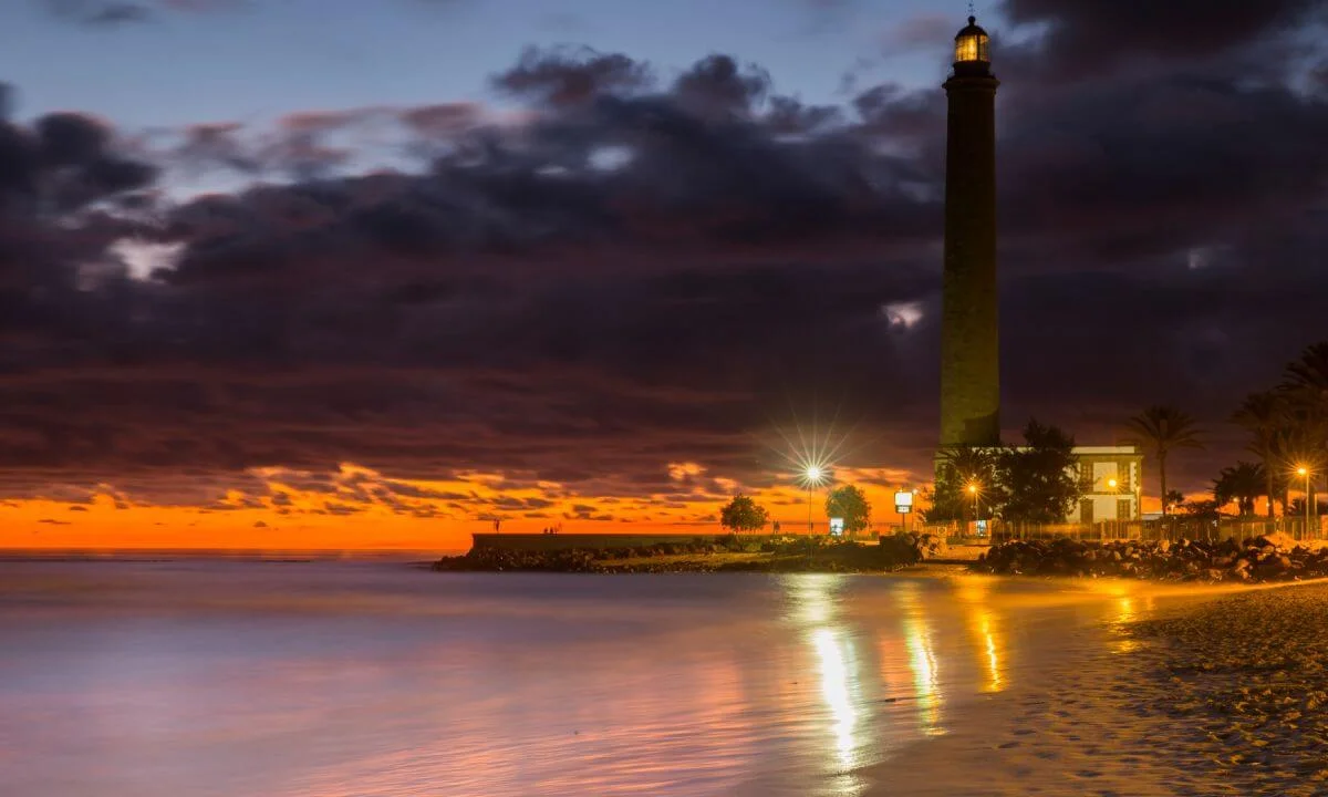 Faro iluminado junto a la costa al atardecer con reflejos en el agua