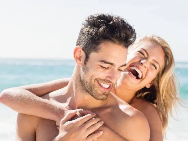 Pareja sonriente en la playa abraz&aacute;ndose, disfrutando del mar