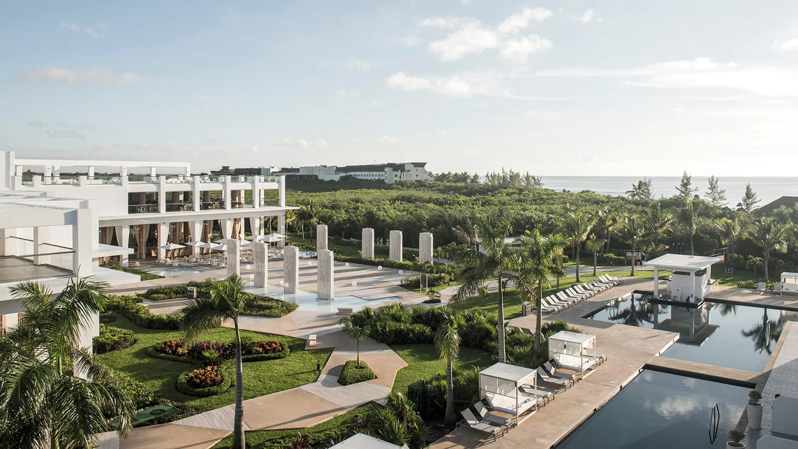 Hotel con jardines tropicales, piscina y vista al mar bajo cielo nublado
